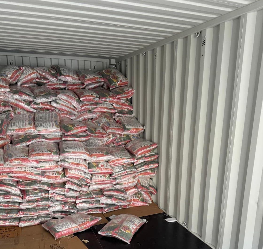 Bags of rice stacked at an angle inside a shipping container, viewed from within.